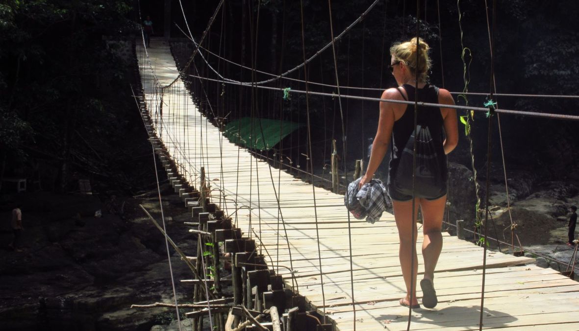 Stimmungsvolle Naturaufnahme. Ein Frau geht im Regenwald über eine Hängebrücke aus Holz. Copyright: echtlebenswert 